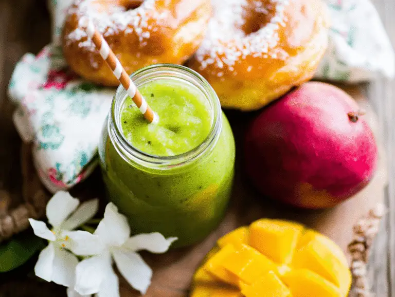 Island Green Smoothie in a mason jar with mango, fresh donut, and tropical flowers on a rustic wooden background